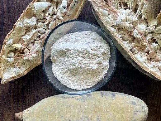 Baobab fruit powder in a glass bowl beside split baobab pods
